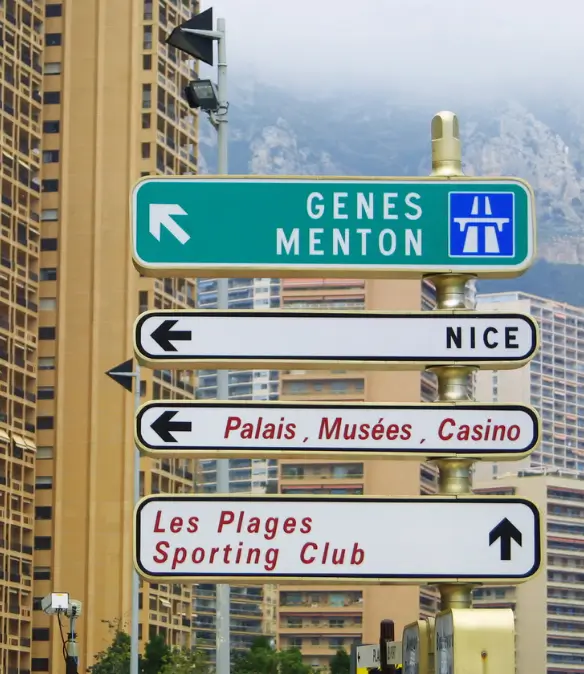 A road sign on a street in Monaco showing nearby amenities and cities on the French Riviera